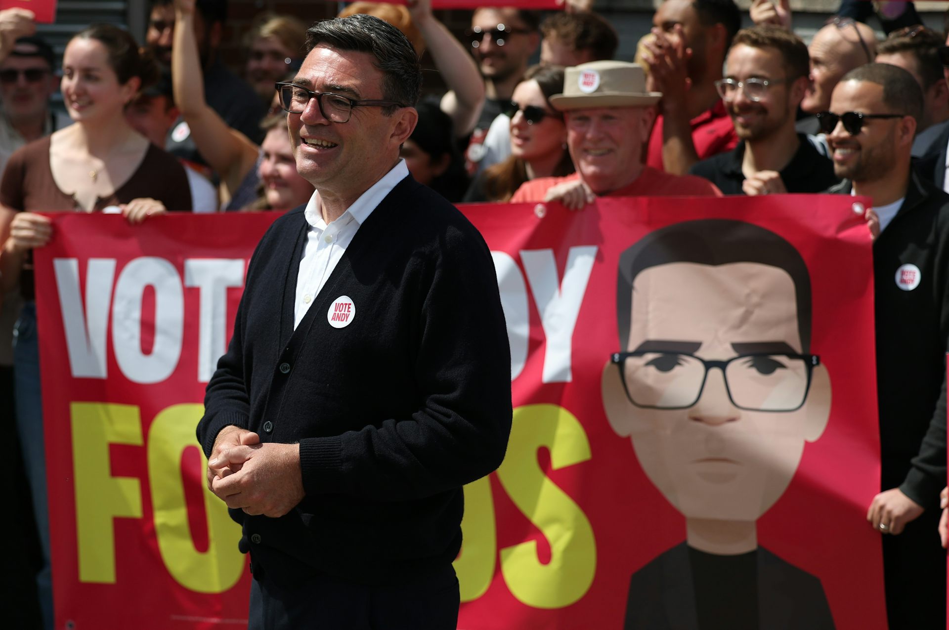 Politician stands with supporters in front of banner