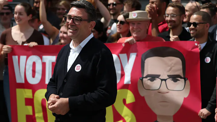 Politician stands with supporters in front of banner