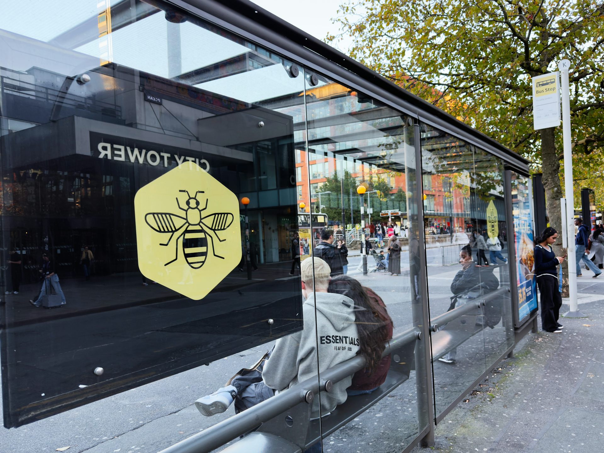 A glass bus shelter with people waiting inside.