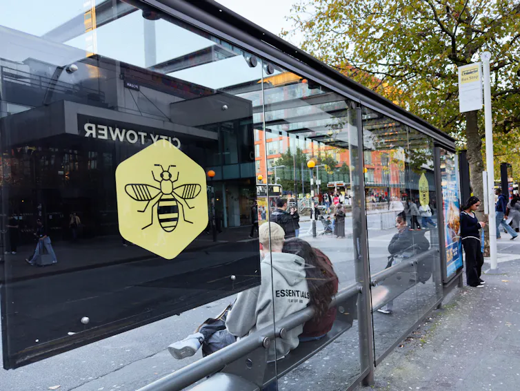 A glass bus shelter with people waiting inside.