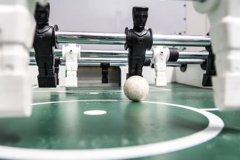 A foosball set with toy figures on metal rods used to propel a small football, a row of black figures on strike, white figures foregrounded.