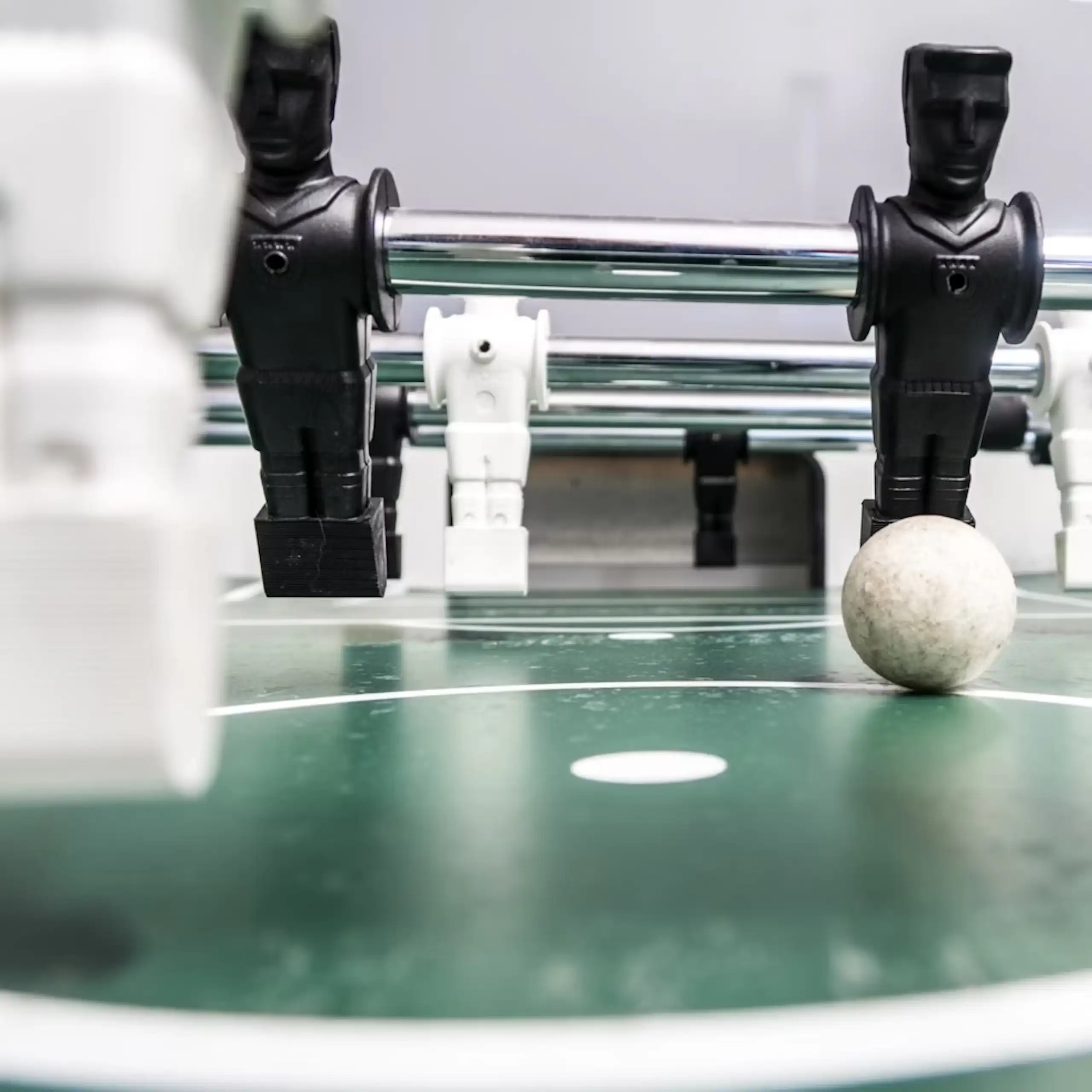A foosball set with toy figures on metal rods used to propel a small football, a row of black figures on strike, white figures foregrounded.