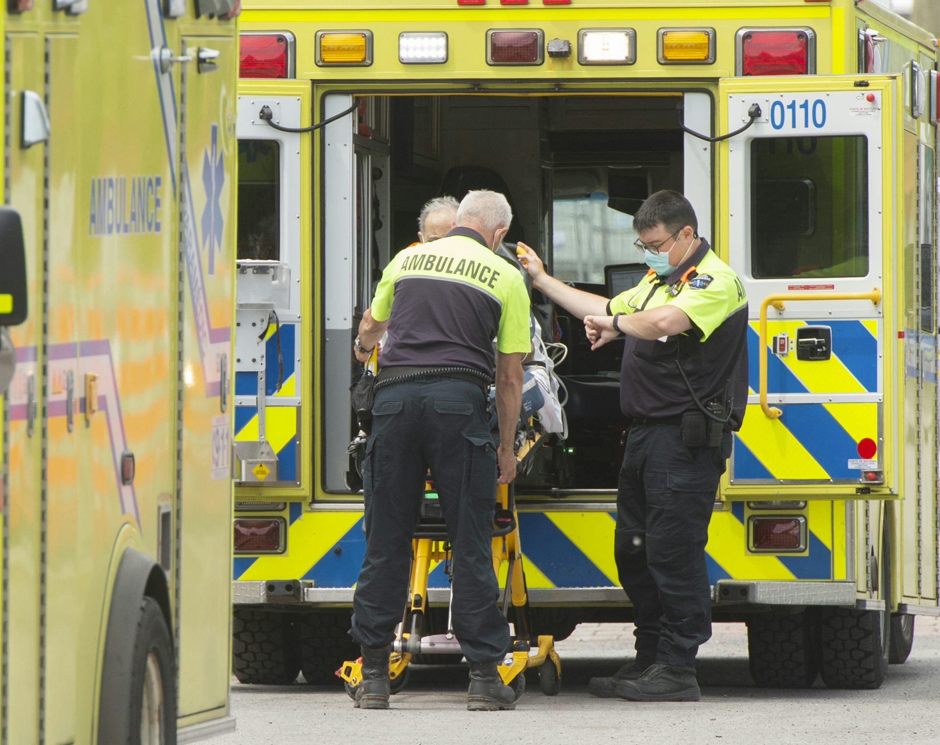 Trois ambulanciers s’apprêtent à embarquer dans une ambulance un patient sur une civière