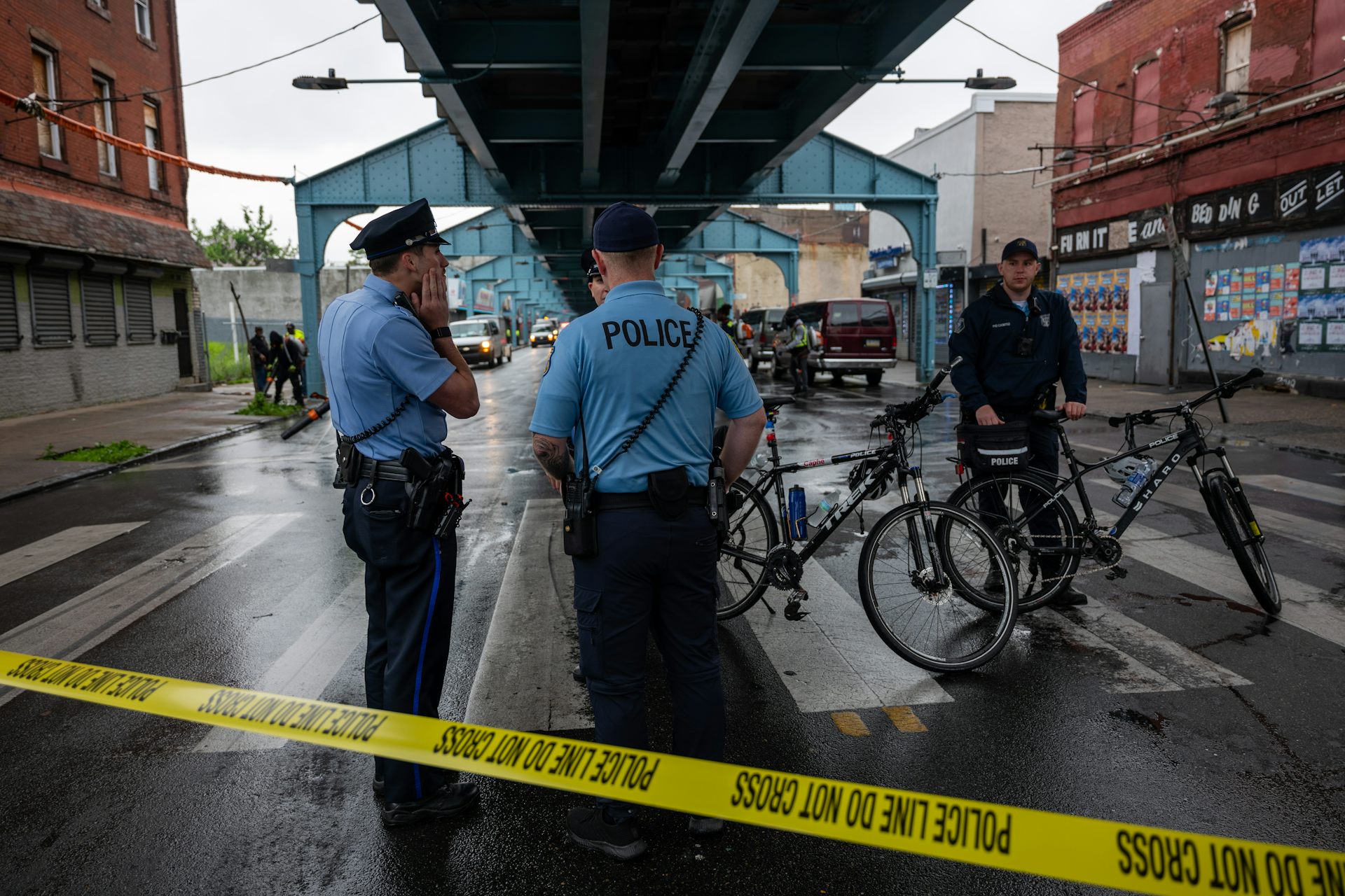 Uniformed police officers gather under underpass behind yellow police tape