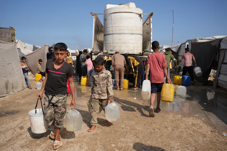 Palestinian boys carry buckets and containers of water away from a water truck.