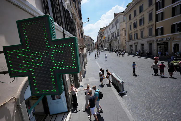A cross-shaped digital sign reads 38 C above a sidewalk