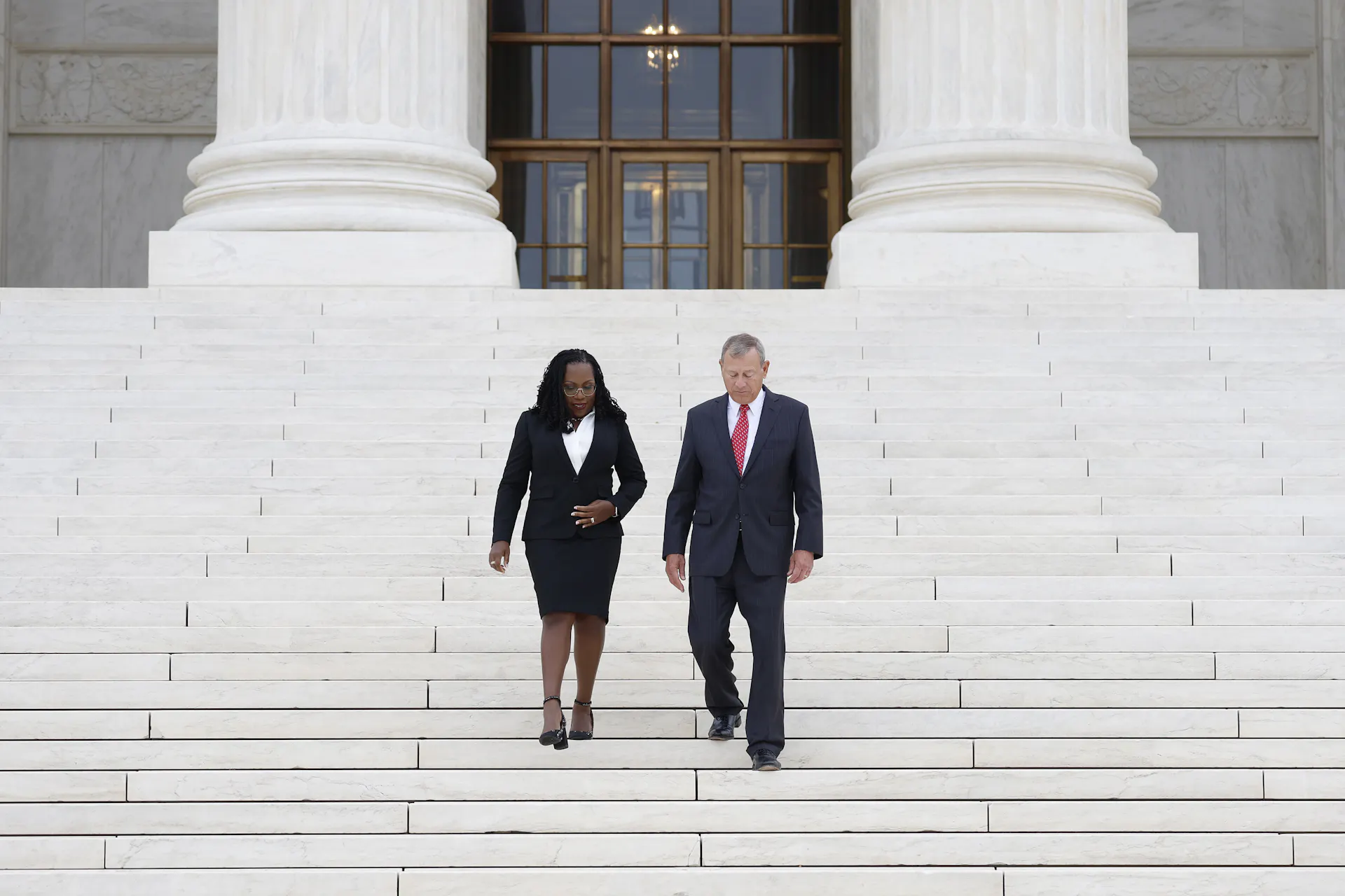 A Black woman and white man walk down steps in front of a federal building.
