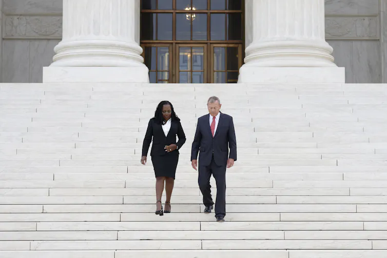A Black woman and white man walk down steps in front of a federal building.