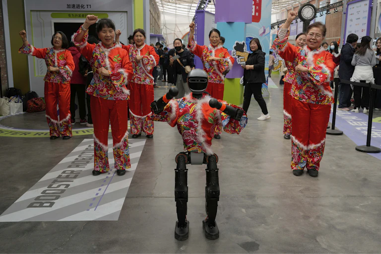 Chinese women wearing traditional red performance clothing raise their arms in dance gestures as they follow a robot