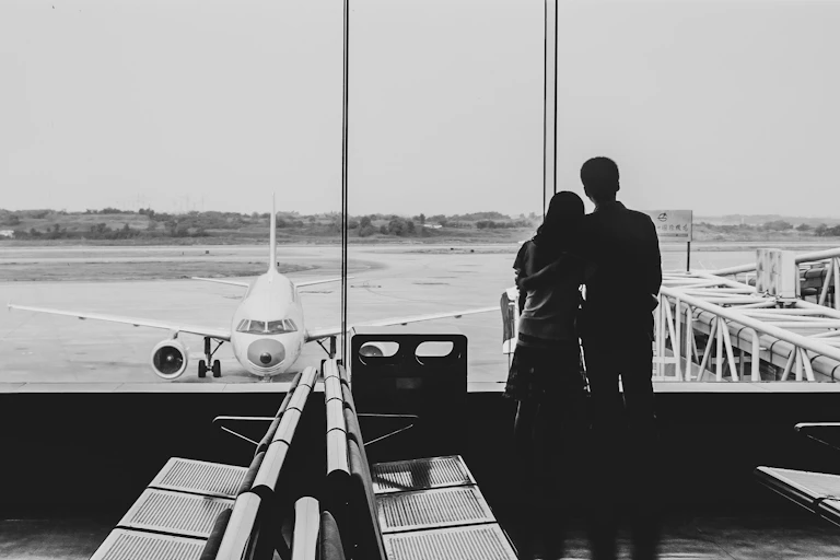 The backs of a couple looking out the window at an airport
