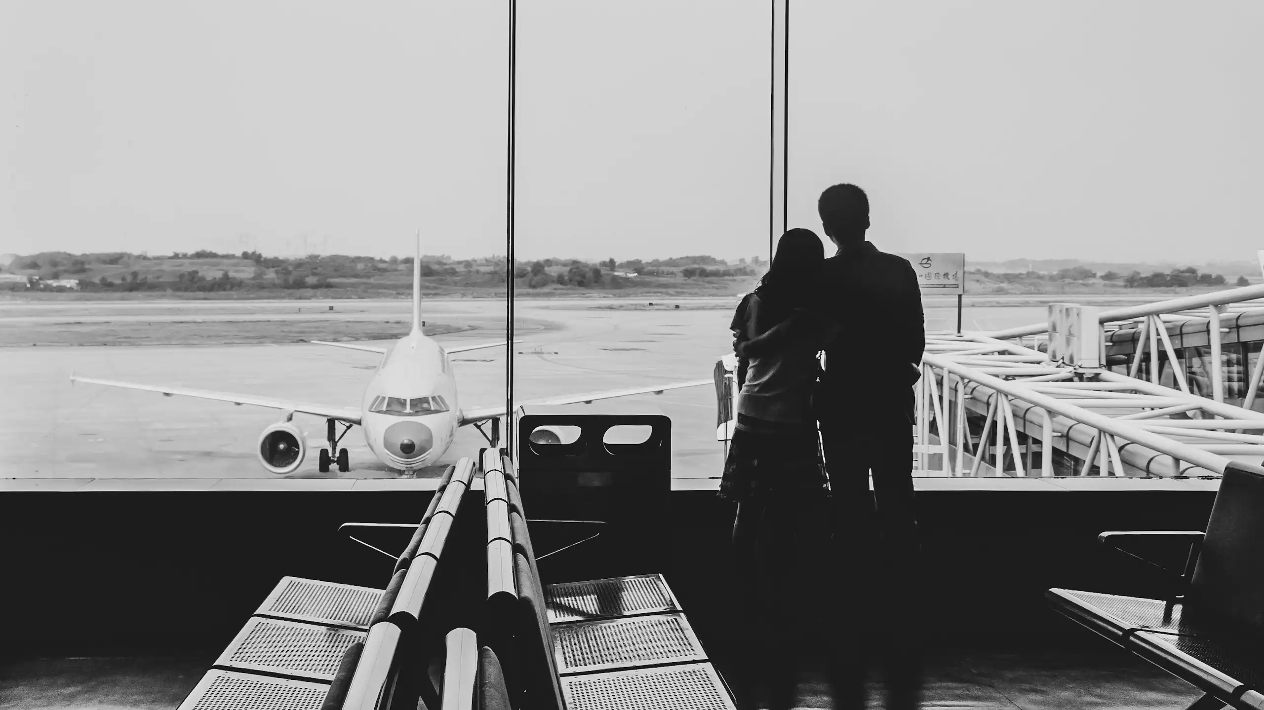 The backs of a couple looking out the window at an airport