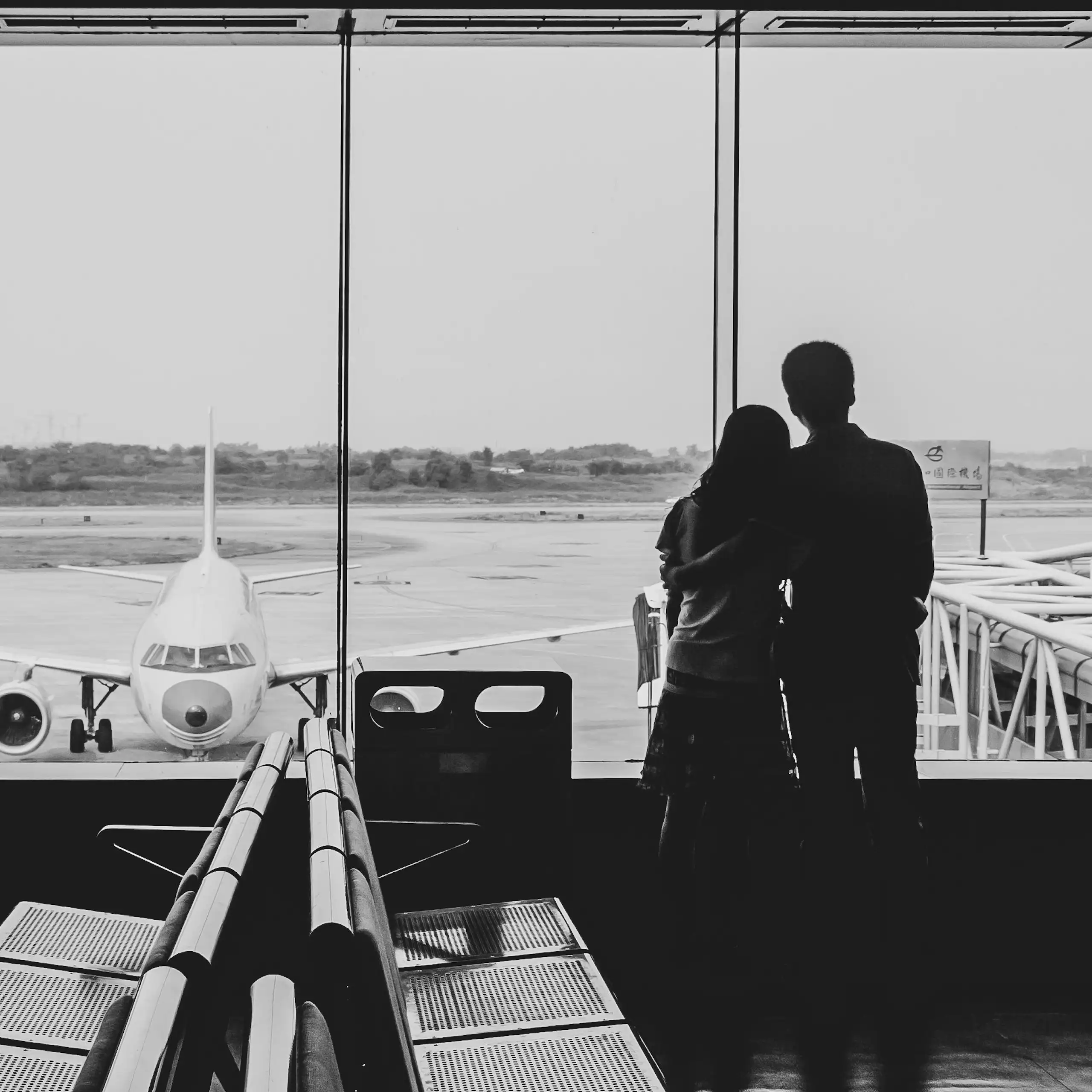 The backs of a couple looking out the window at an airport