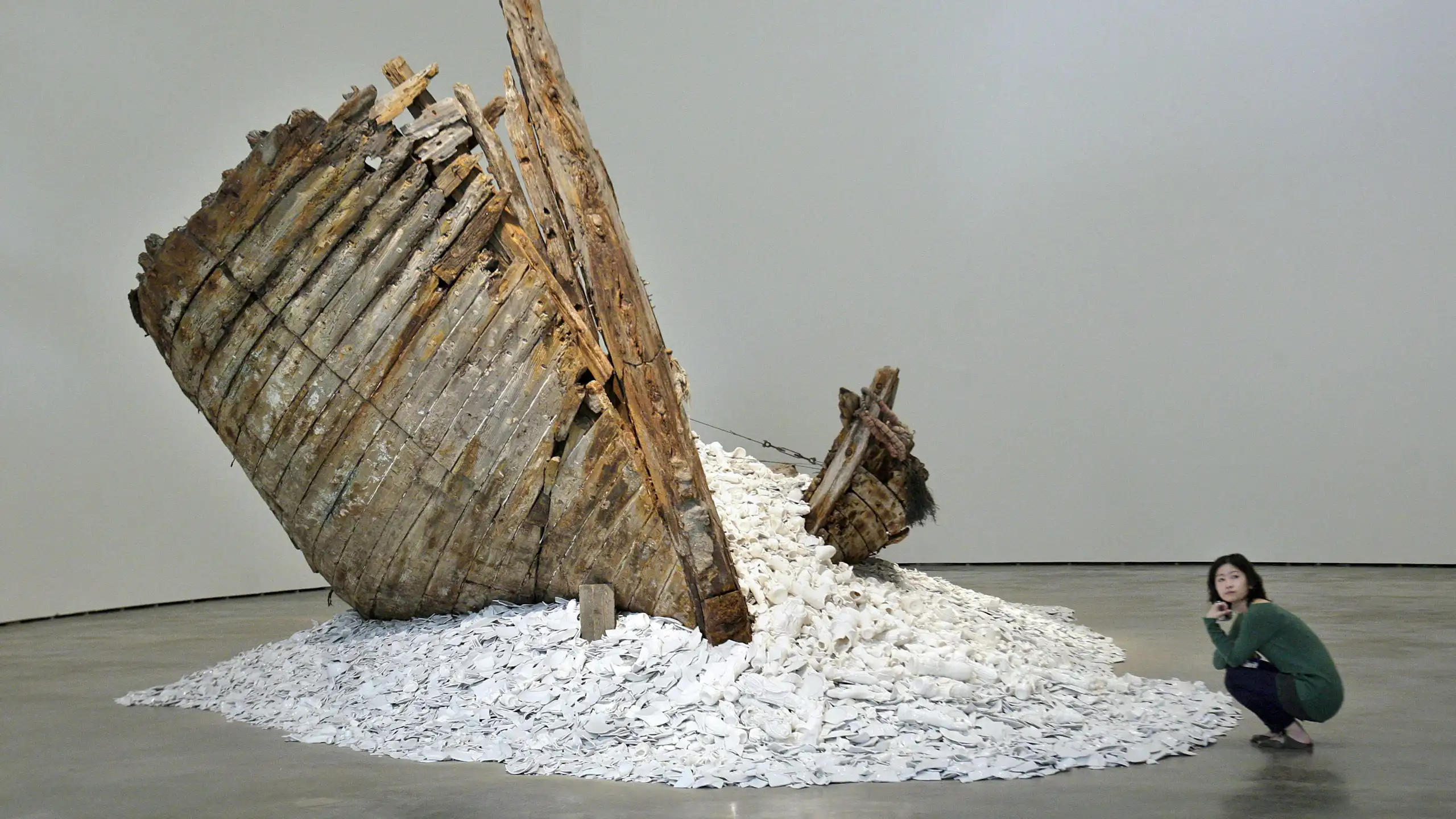 A woman squats next to a sculpture featuring a ship wreckage and pieces of porcelain.