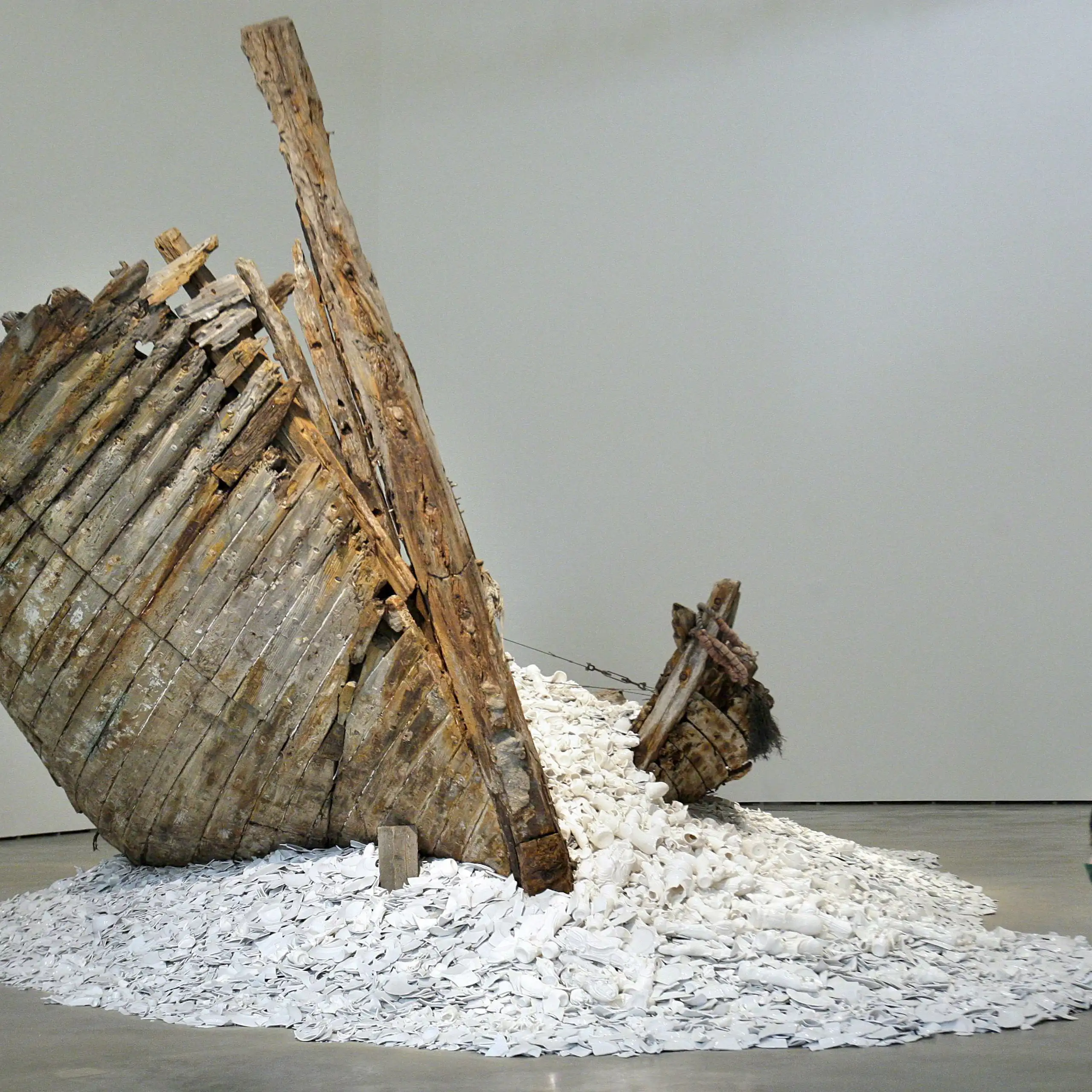 A woman squats next to a sculpture featuring a ship wreckage and pieces of porcelain.