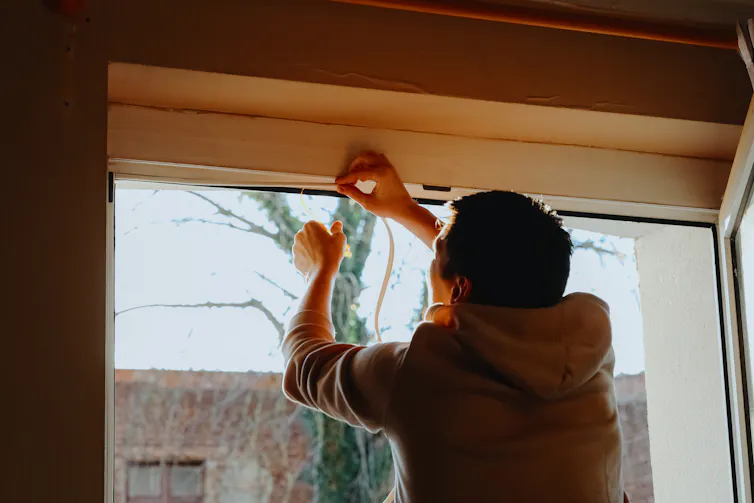 man installs a draught stopper around a window inside his house.