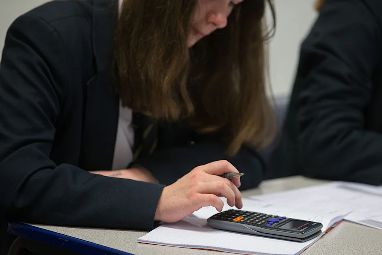 A teenage girl in school uniform uses a calculator during class.