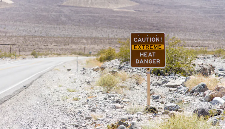 A sign warning visitors of extreme heat is posted next to a road in a rocky desert