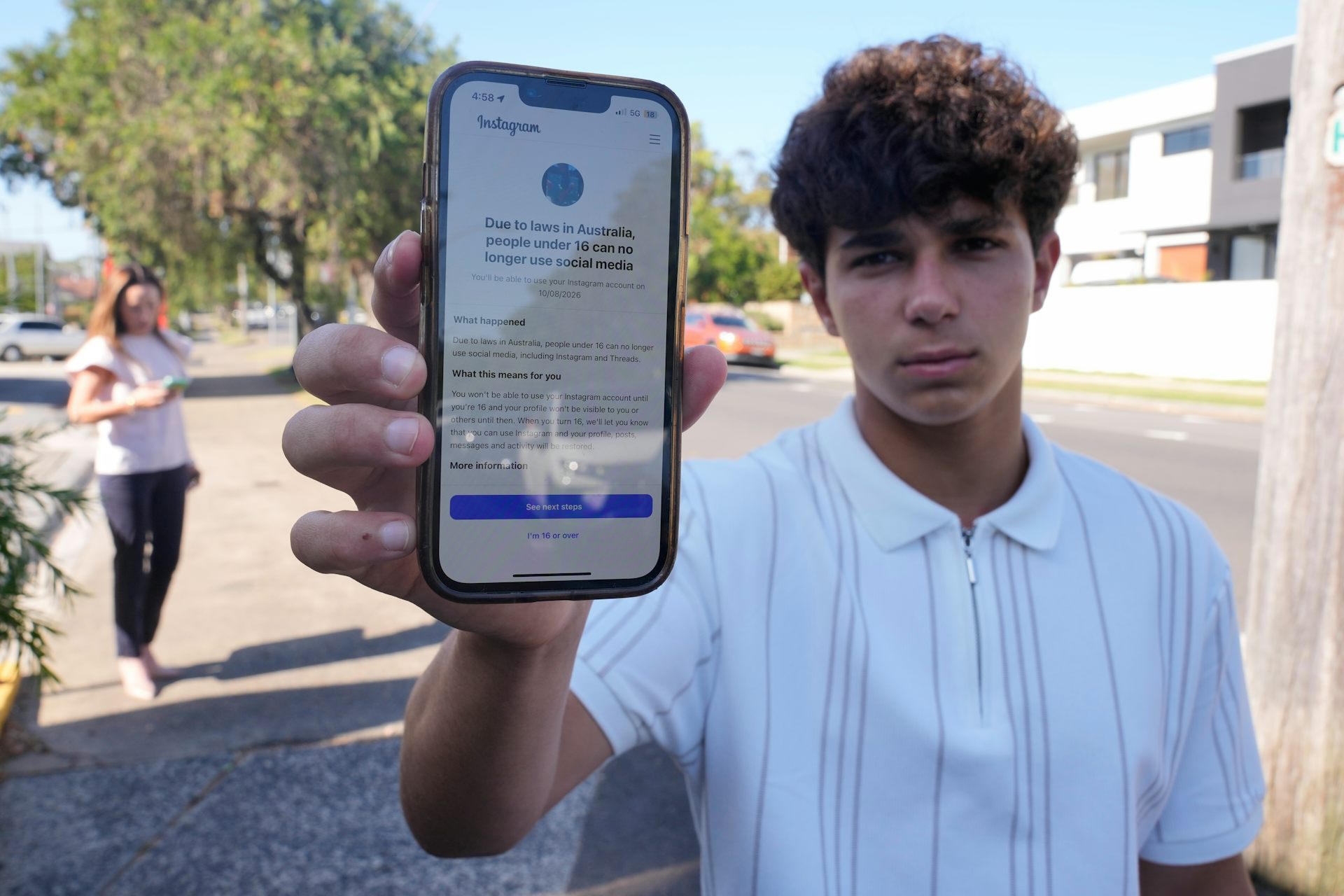 Un adolescent montre l'écran de son téléphone, sur lequel s'affiche un avis indiquant qu'Instagram est inaccessible aux moins de 16 ans.