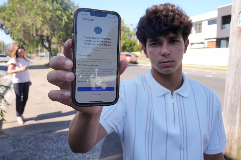 Un adolescent montre l'écran de son téléphone, sur lequel s'affiche un avis indiquant qu'Instagram est inaccessible aux moins de 16 ans.
