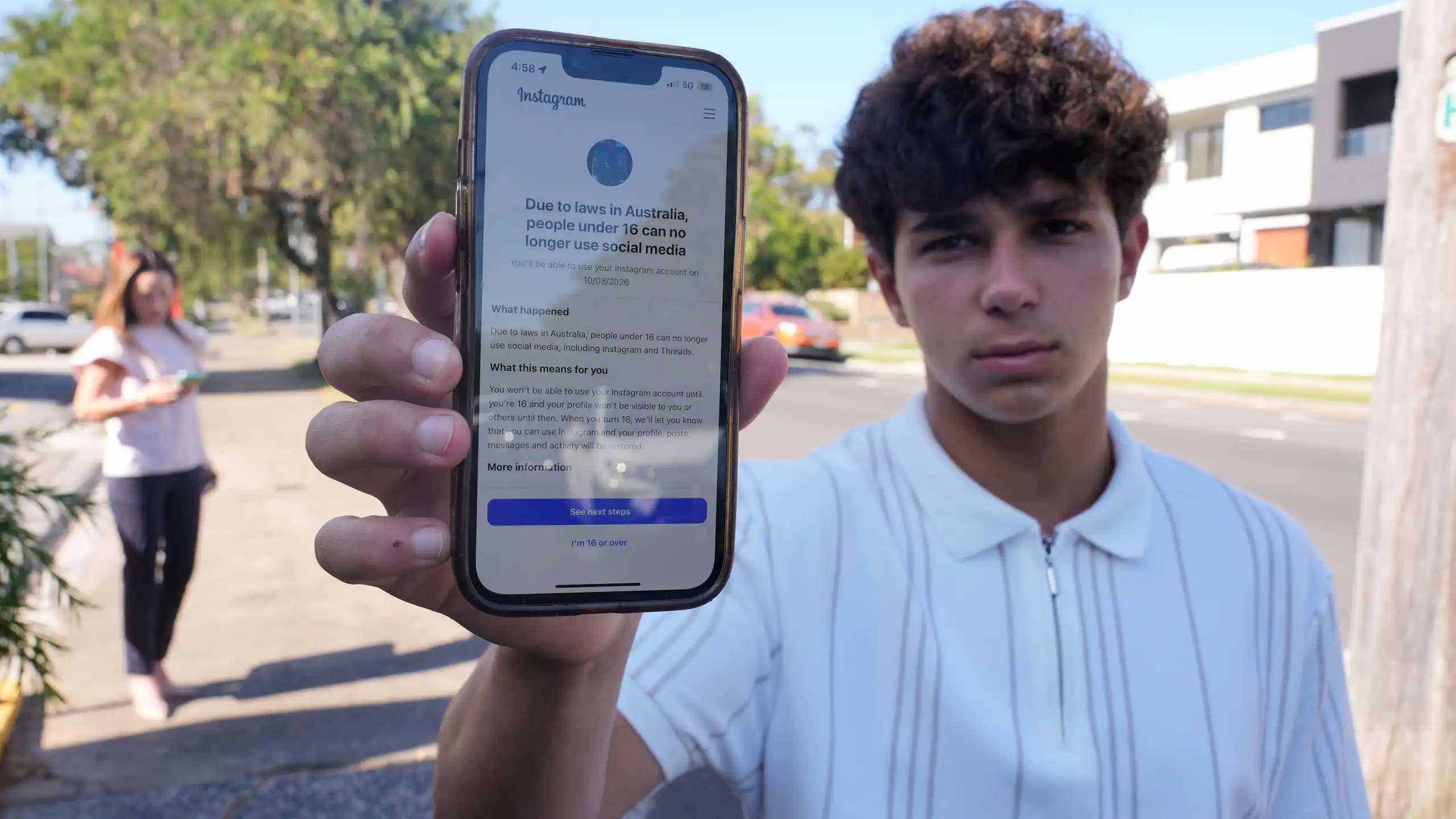 Un adolescent montre l'écran de son téléphone, sur lequel s'affiche un avis indiquant qu'Instagram est inaccessible aux moins de 16 ans.