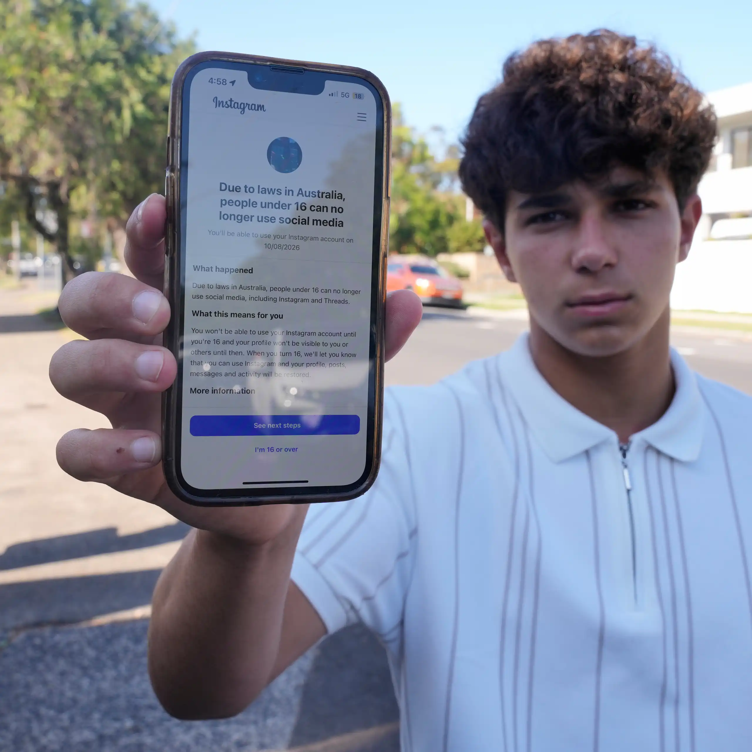 Un adolescent montre l'écran de son téléphone, sur lequel s'affiche un avis indiquant qu'Instagram est inaccessible aux moins de 16 ans.