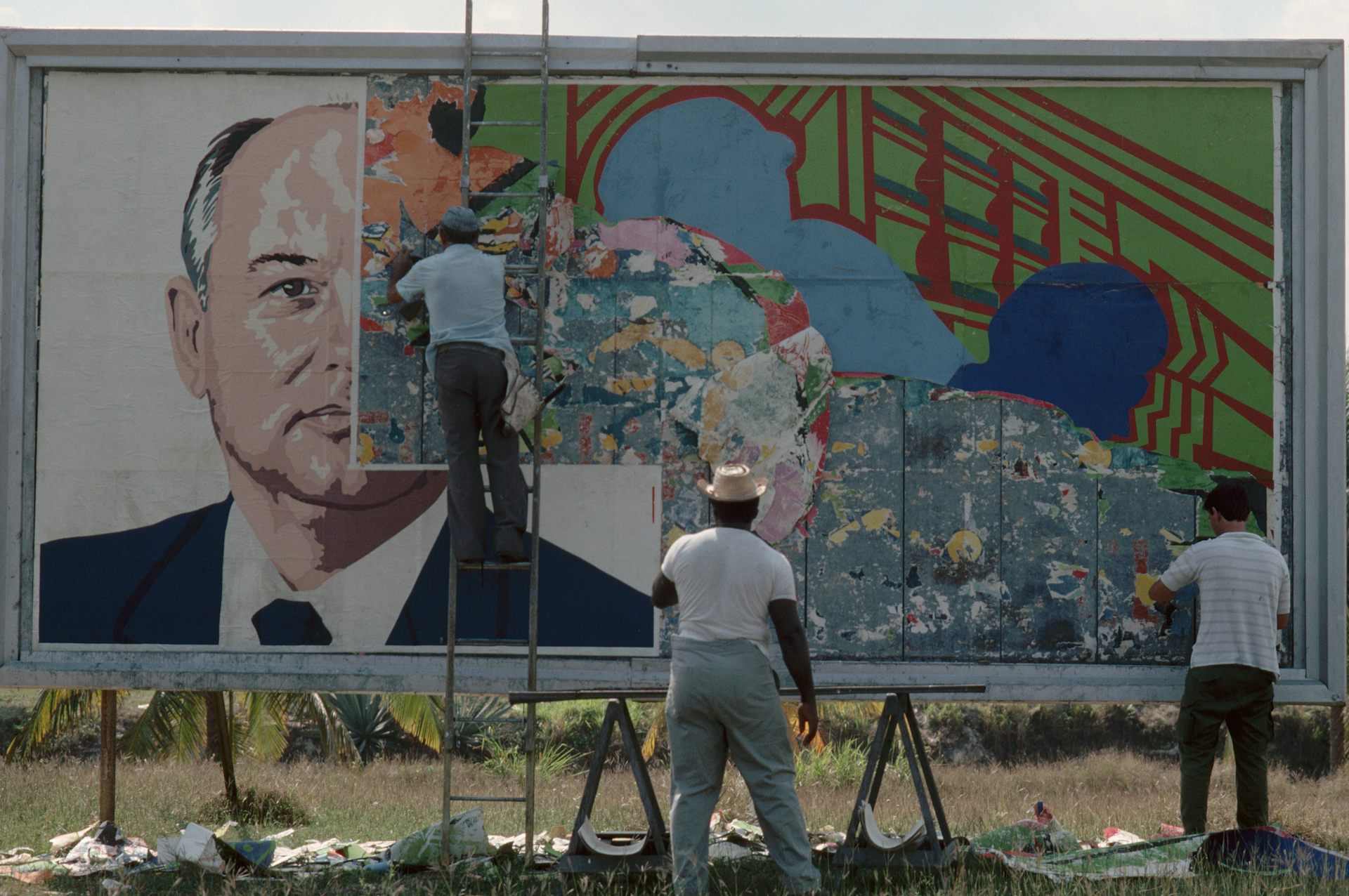 Two men paste over the image of a man on a billboard