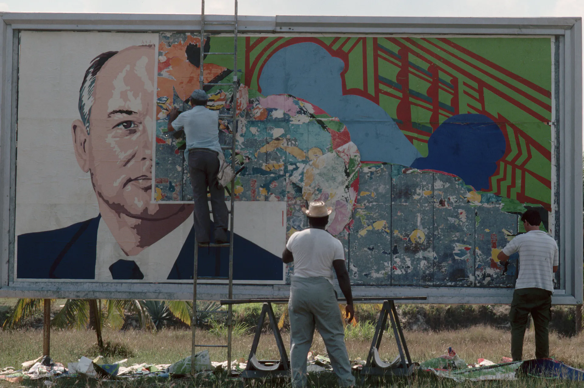 Two men paste over the image of a man on a billboard