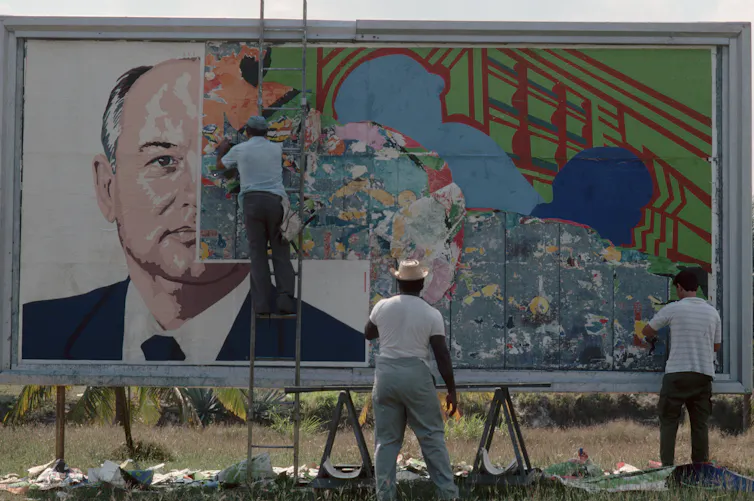 Two men paste over the image of a man on a billboard