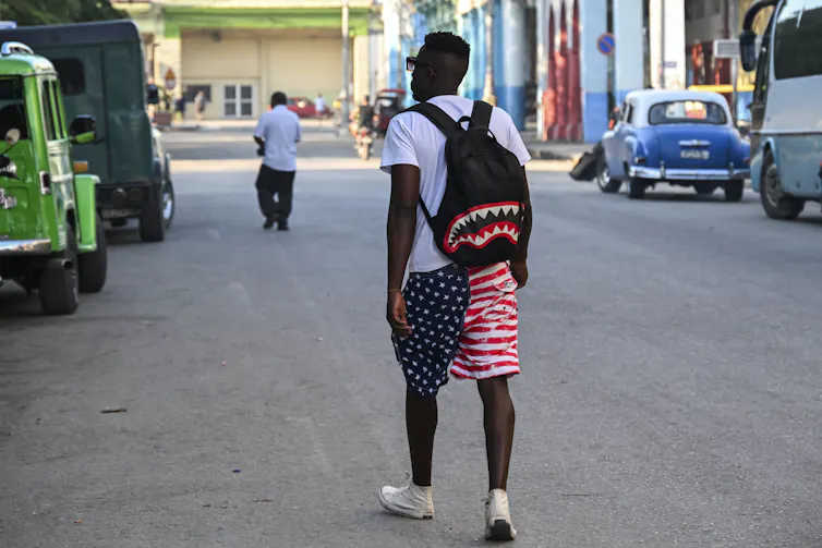 A man wears a backpack and red, white and blue shorts.