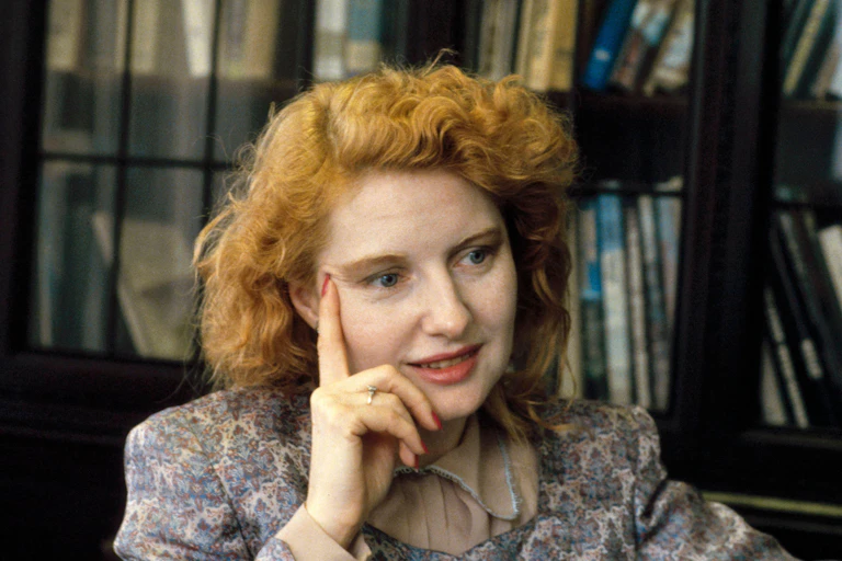 A woman with red hair sitting in front of a bookcase