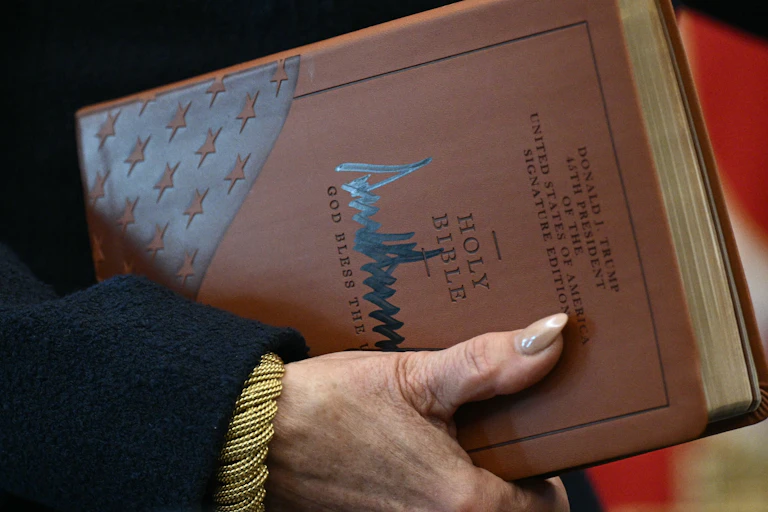 Gros plan sur les mains de la procureure tenant la Bible et la signature de Trump sur la couverture.