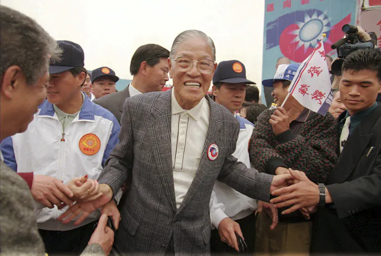 Hombre asiático mayor sonriente entre la multitud de personas.