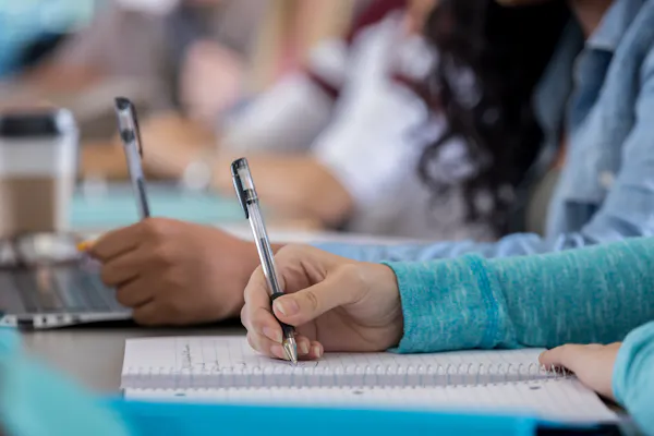 Several people's hands are seen holding pens and leaning over white notebooks.