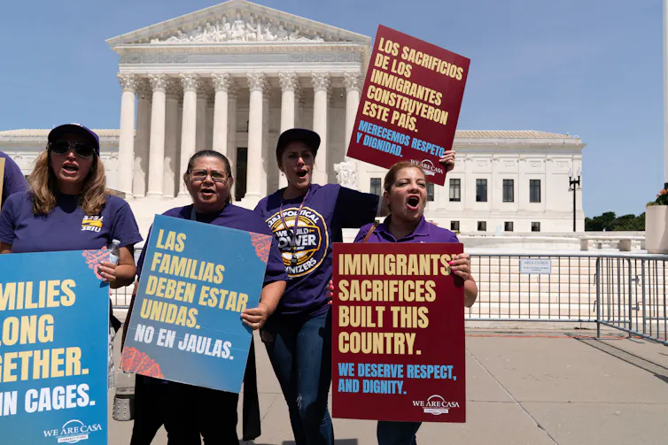 People carry signs advocating for birthright citizenship in front of an ornate stone building.
