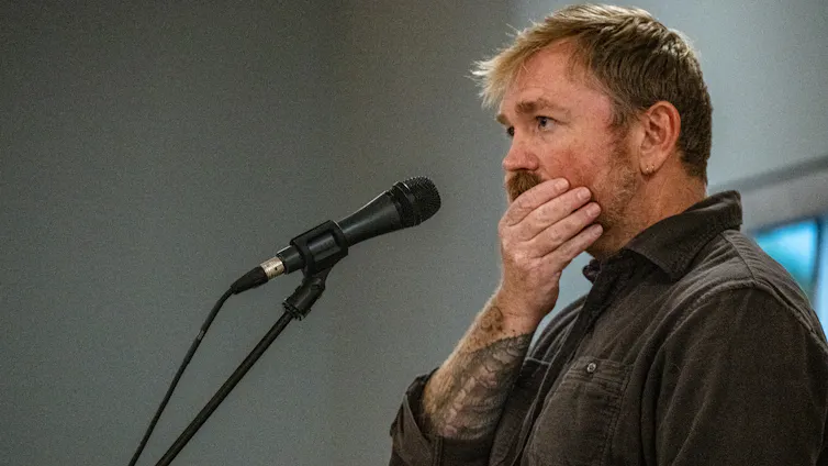 A rusty-haired man rubbing his face in front of a microphone.