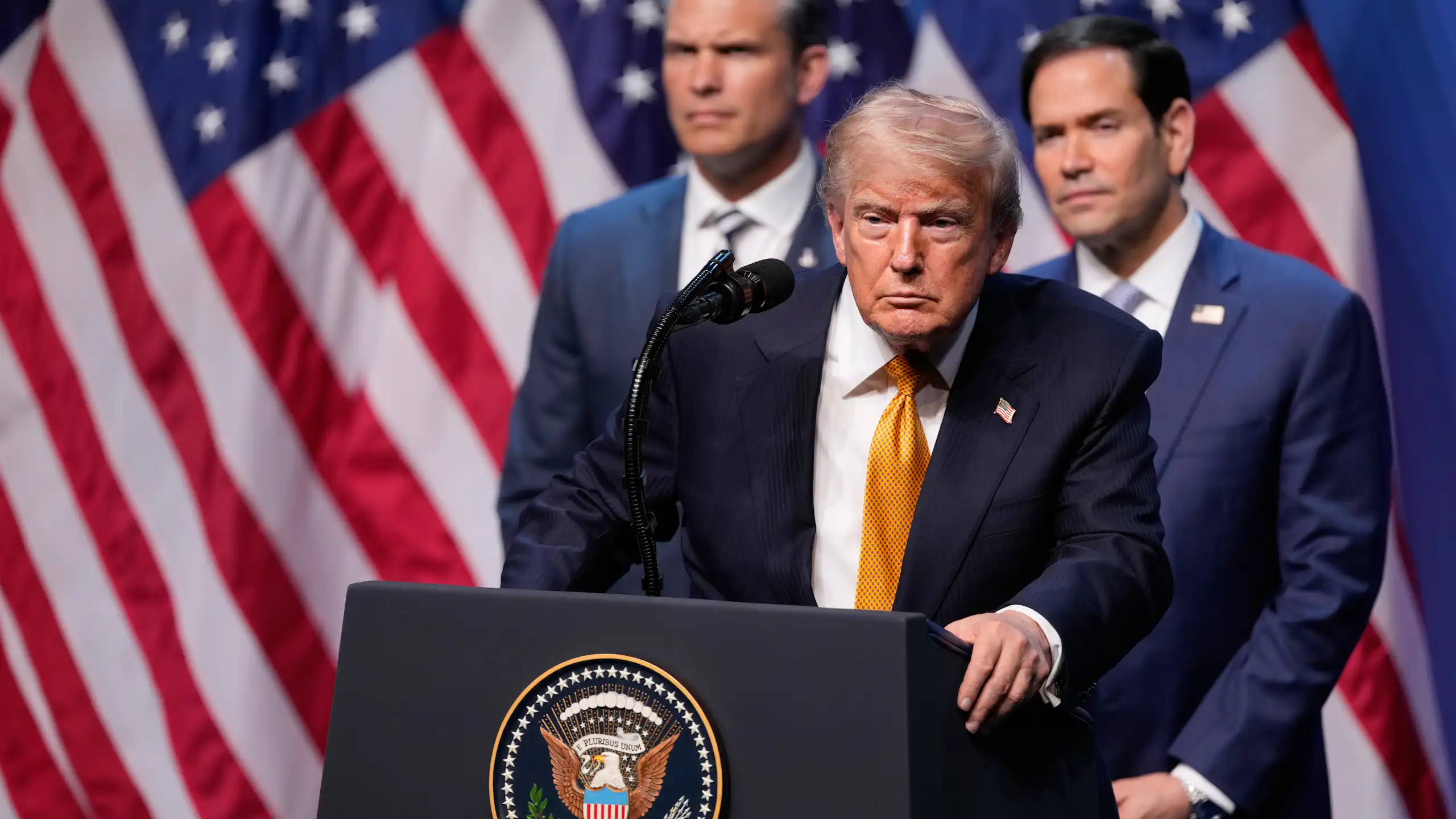 Donald Trump stands at lectern bearing presidential seal with Pete Hegseth, Marco Rubio and US flags behind him