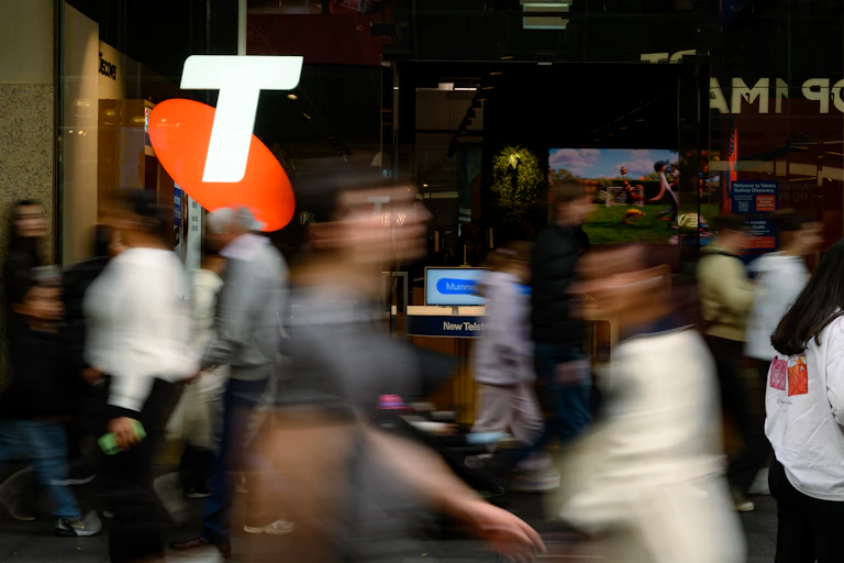 People stream past an orange and white Telstra logo.