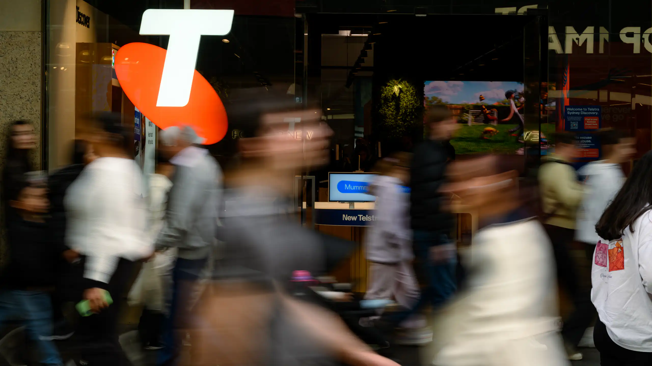 People stream past an orange and white Telstra logo.