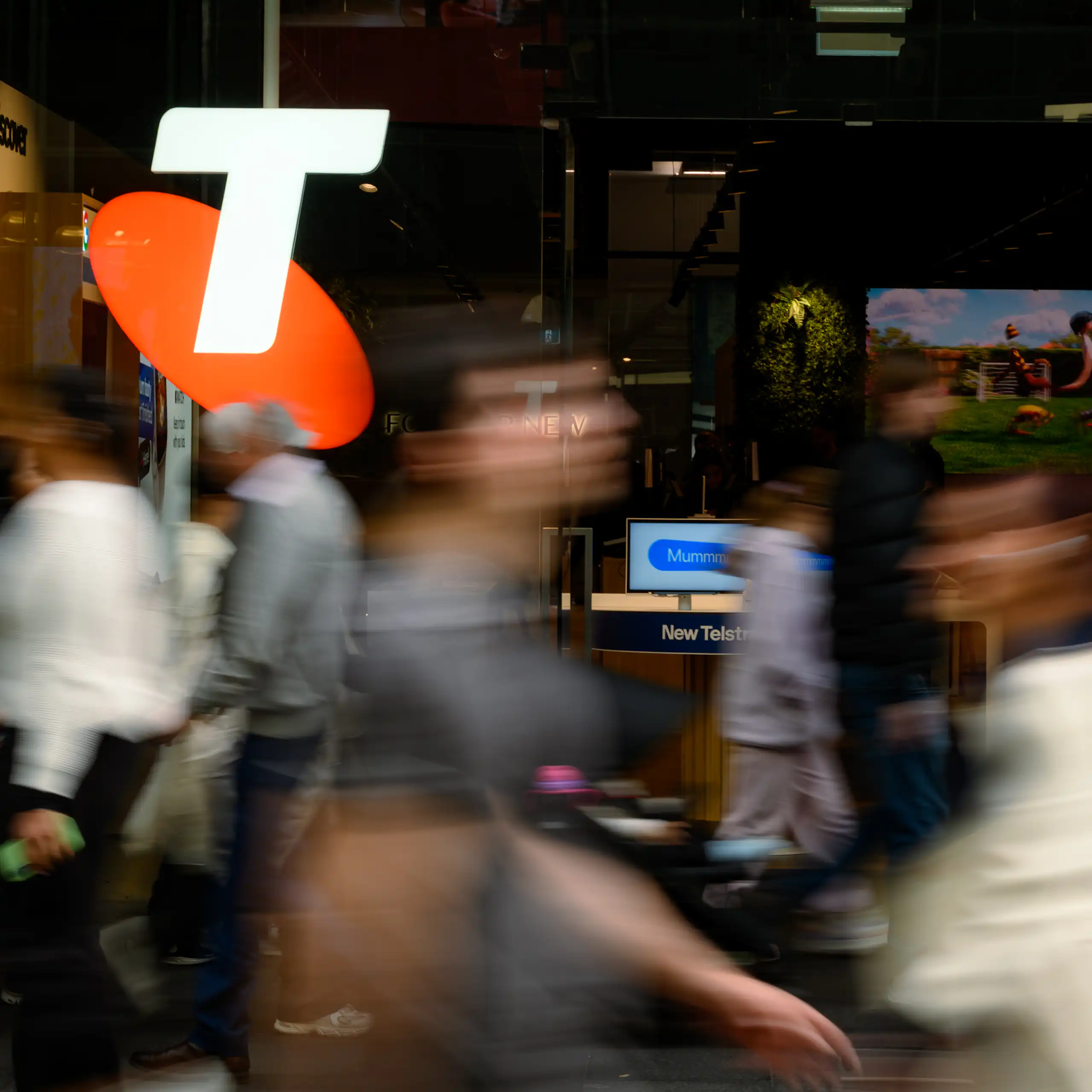 People stream past an orange and white Telstra logo.