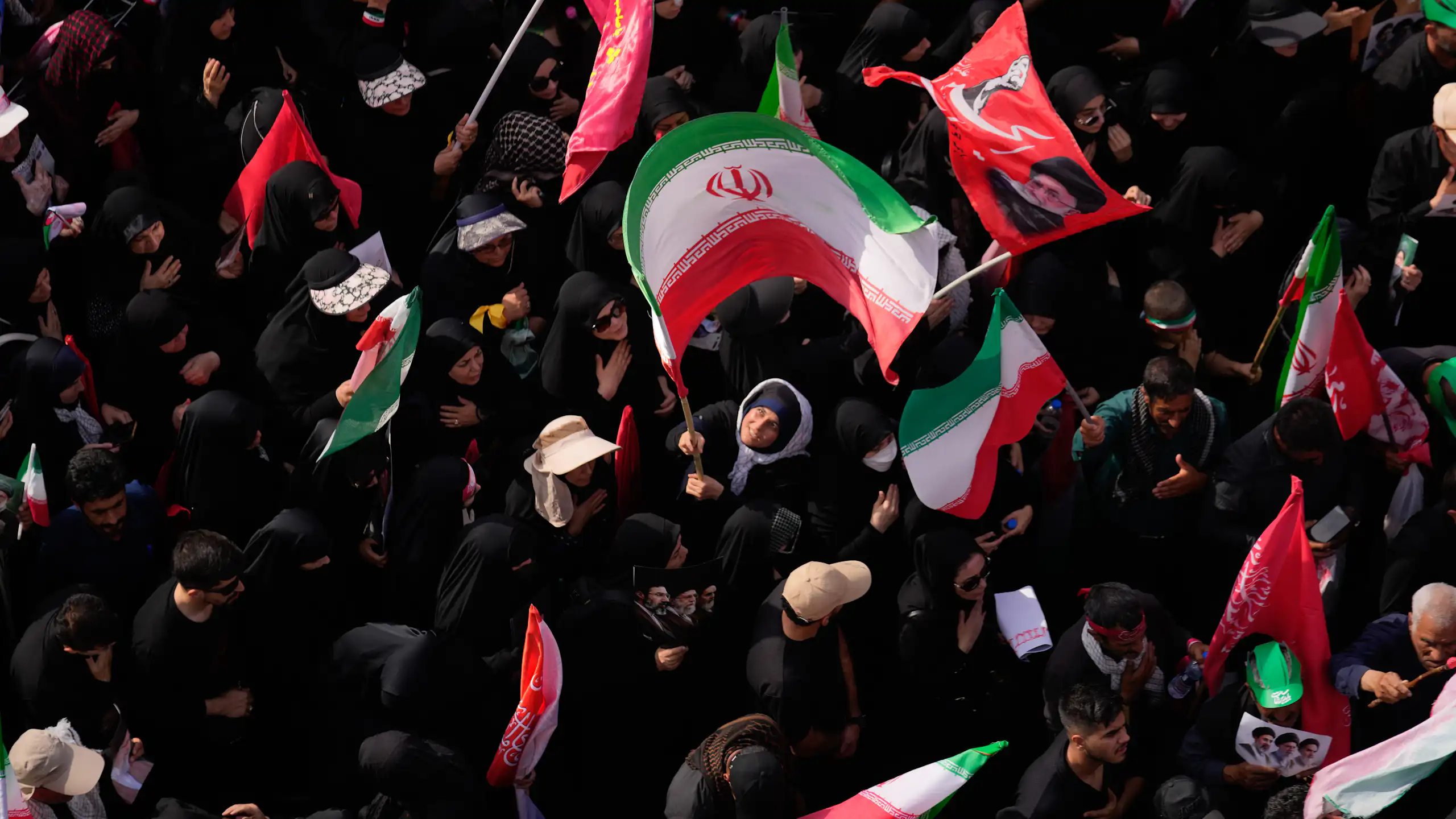 A woman waves a large Iranian flag in a dense crowd