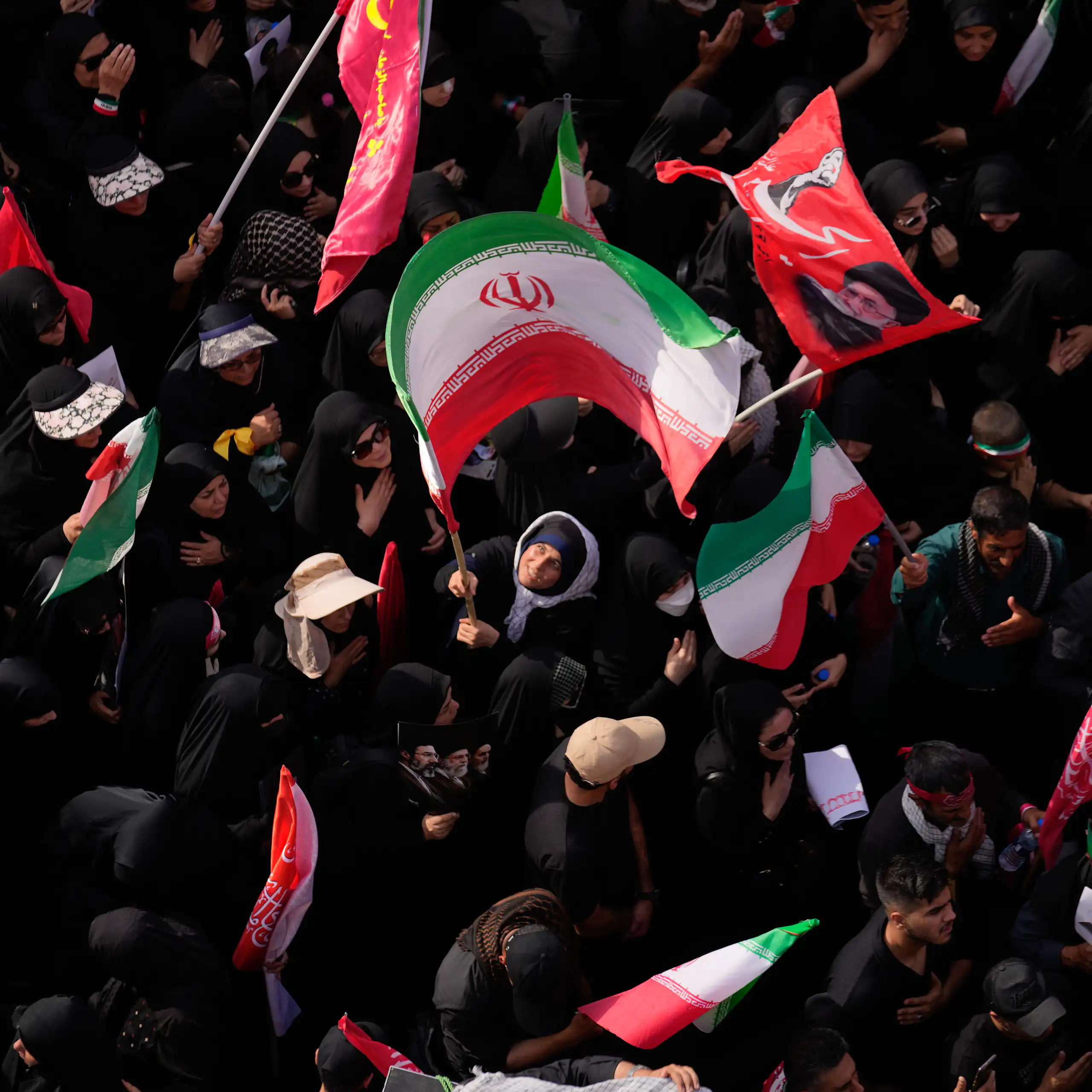 A woman waves a large Iranian flag in a dense crowd