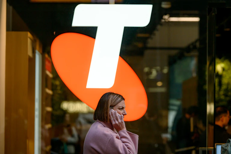 Woman on phone walks under Telstra sign.