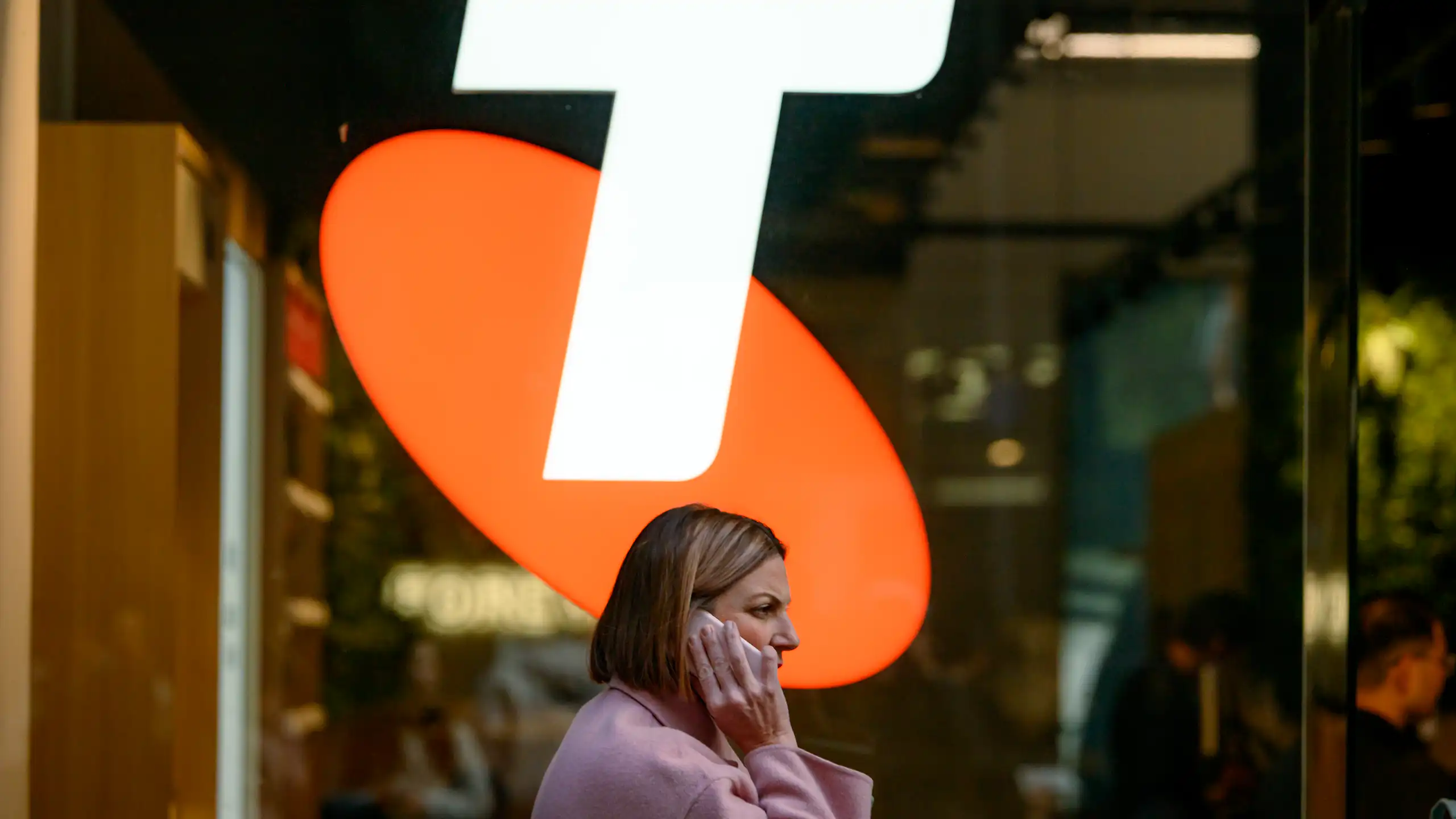 Woman on phone walks under Telstra sign.