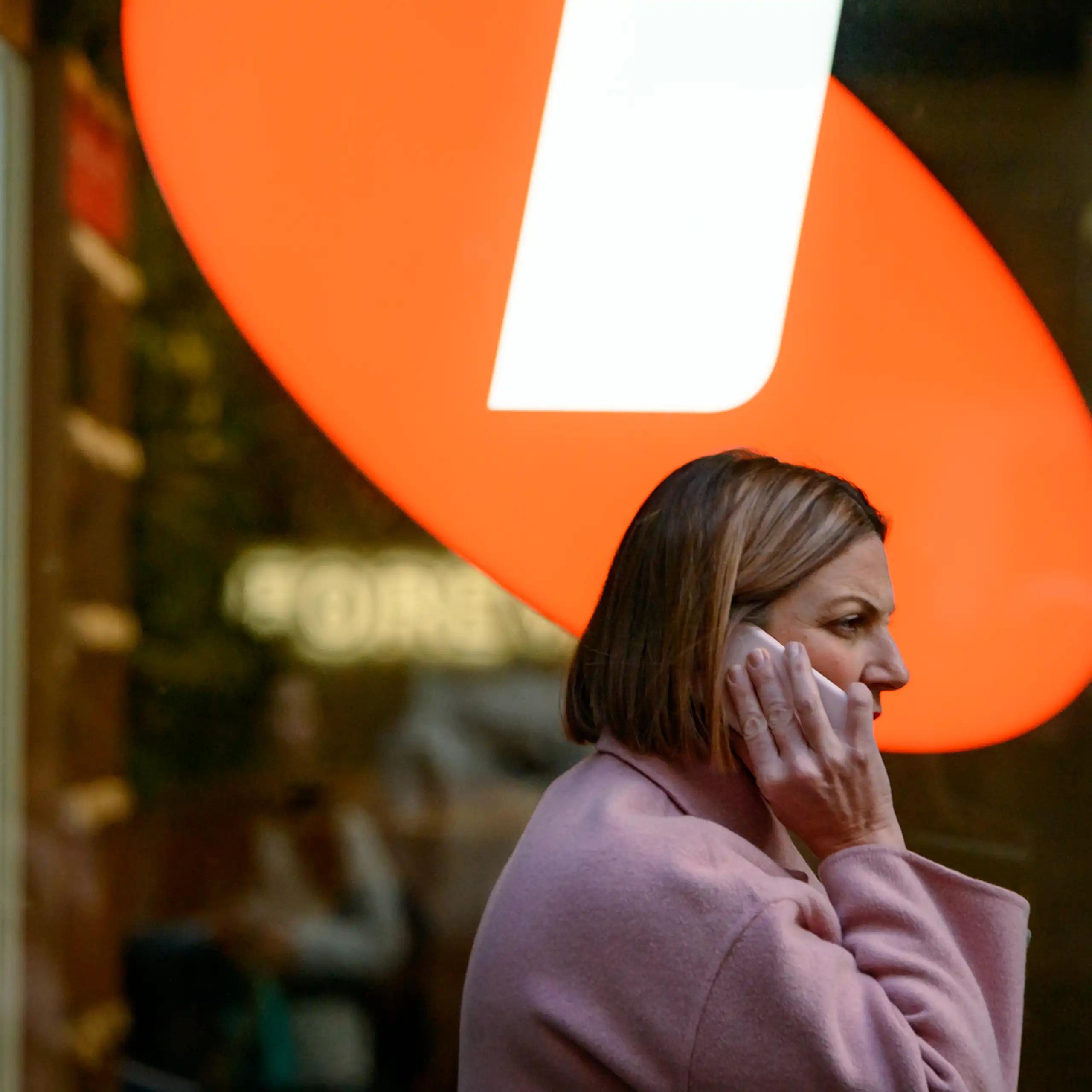 Woman on phone walks under Telstra sign.