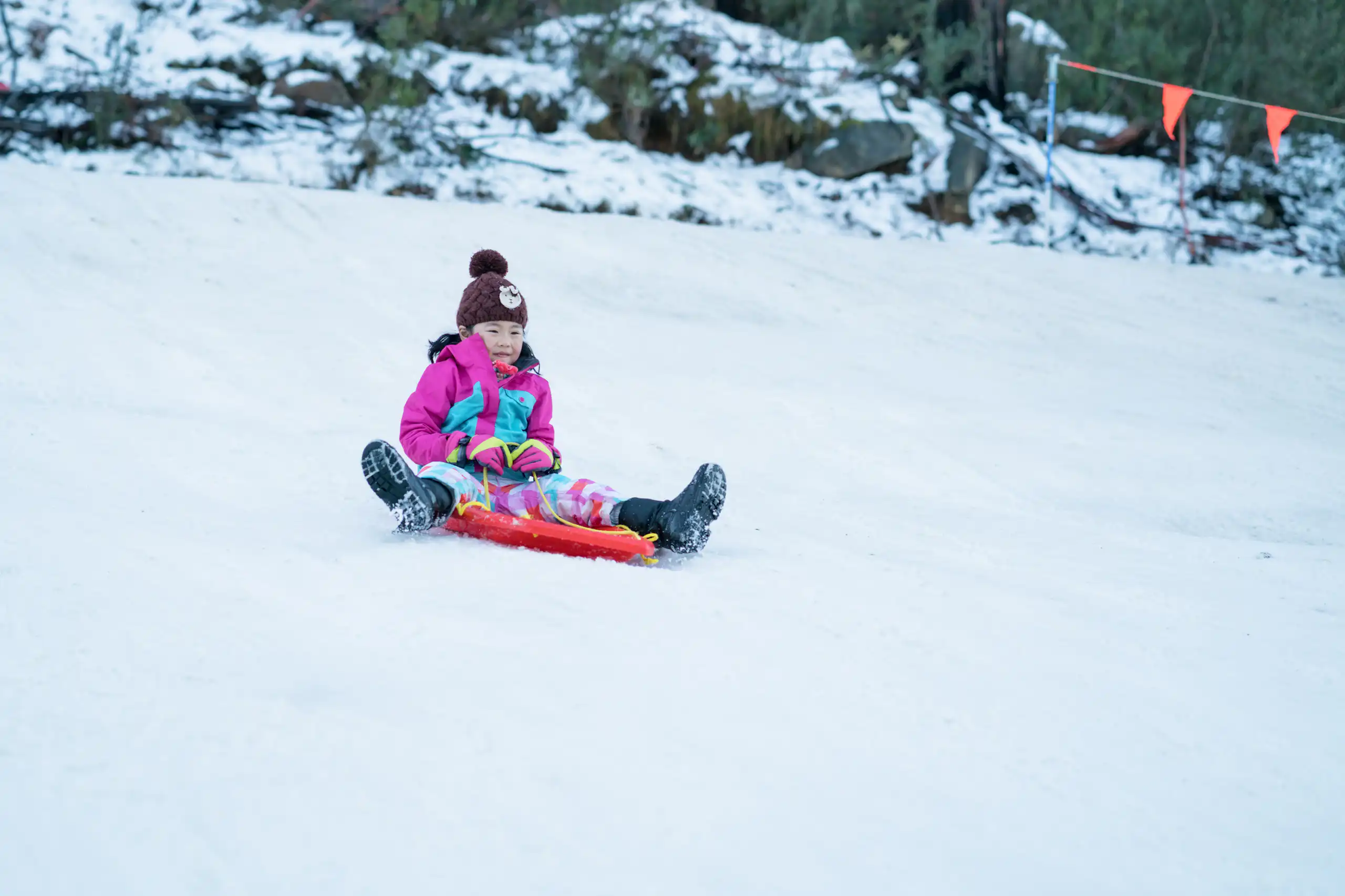 Young girl slides down a snowy mountain on a red toboggan.