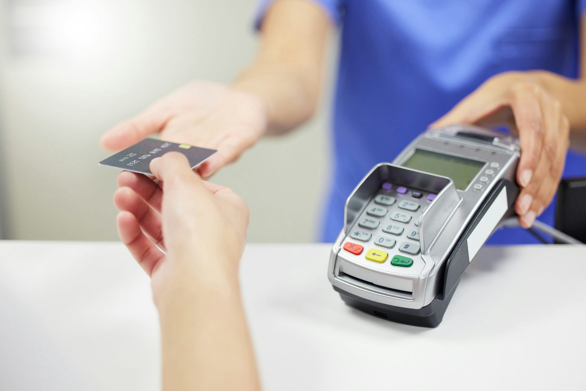 Une soignante tend un terminal de paiement à une patiente pour un règlement par carte bleue.