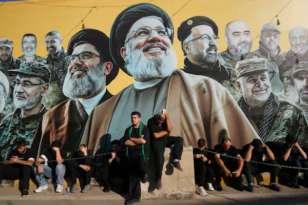 Several men sit below a large mural.