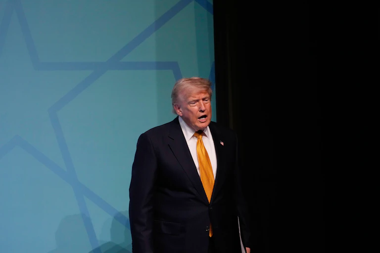A rotund, sleepy-looking older man in a baggy suit and shaggy orange-ish white hair.