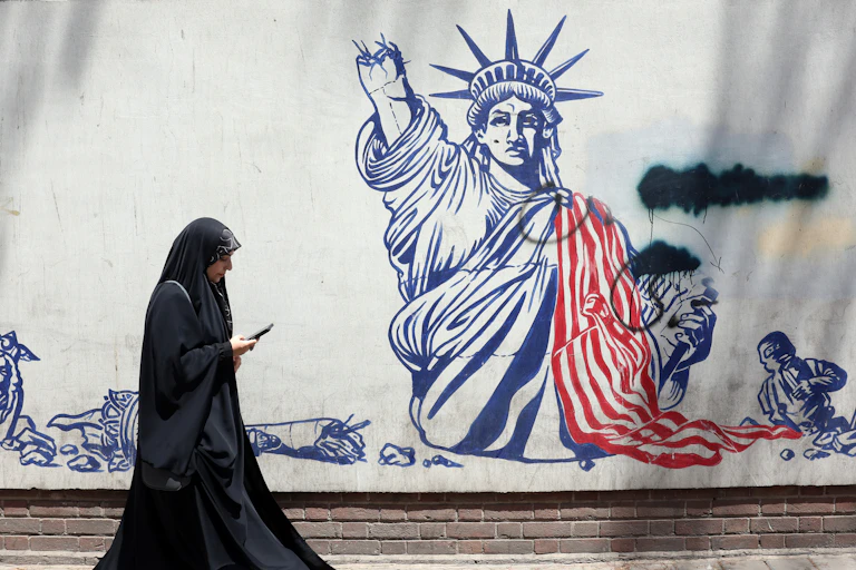 A woman i a burqa walks past an anti-US Mural