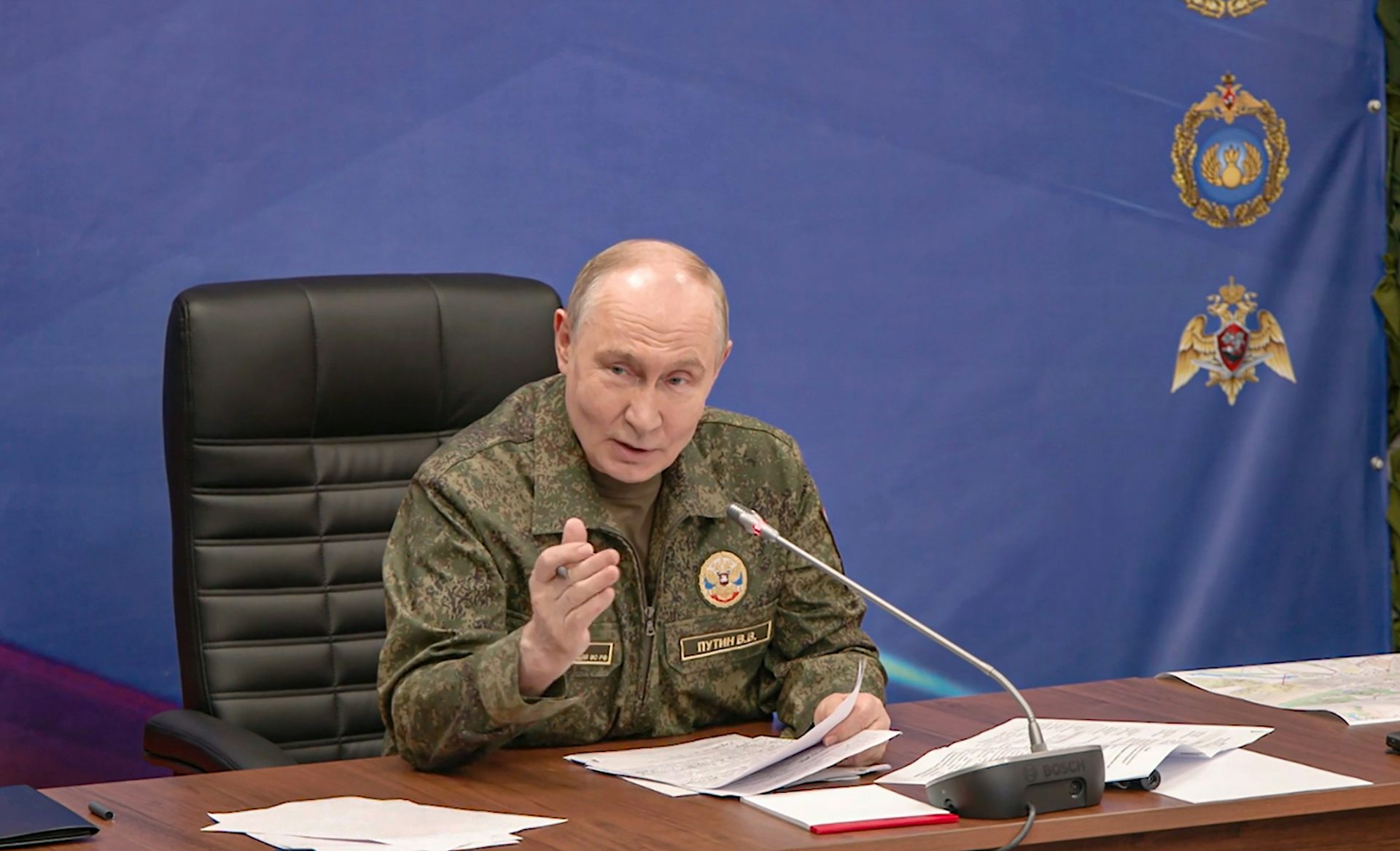 Russian president, Vladimir Putin, weating a military uniform and sitting behind a desk.